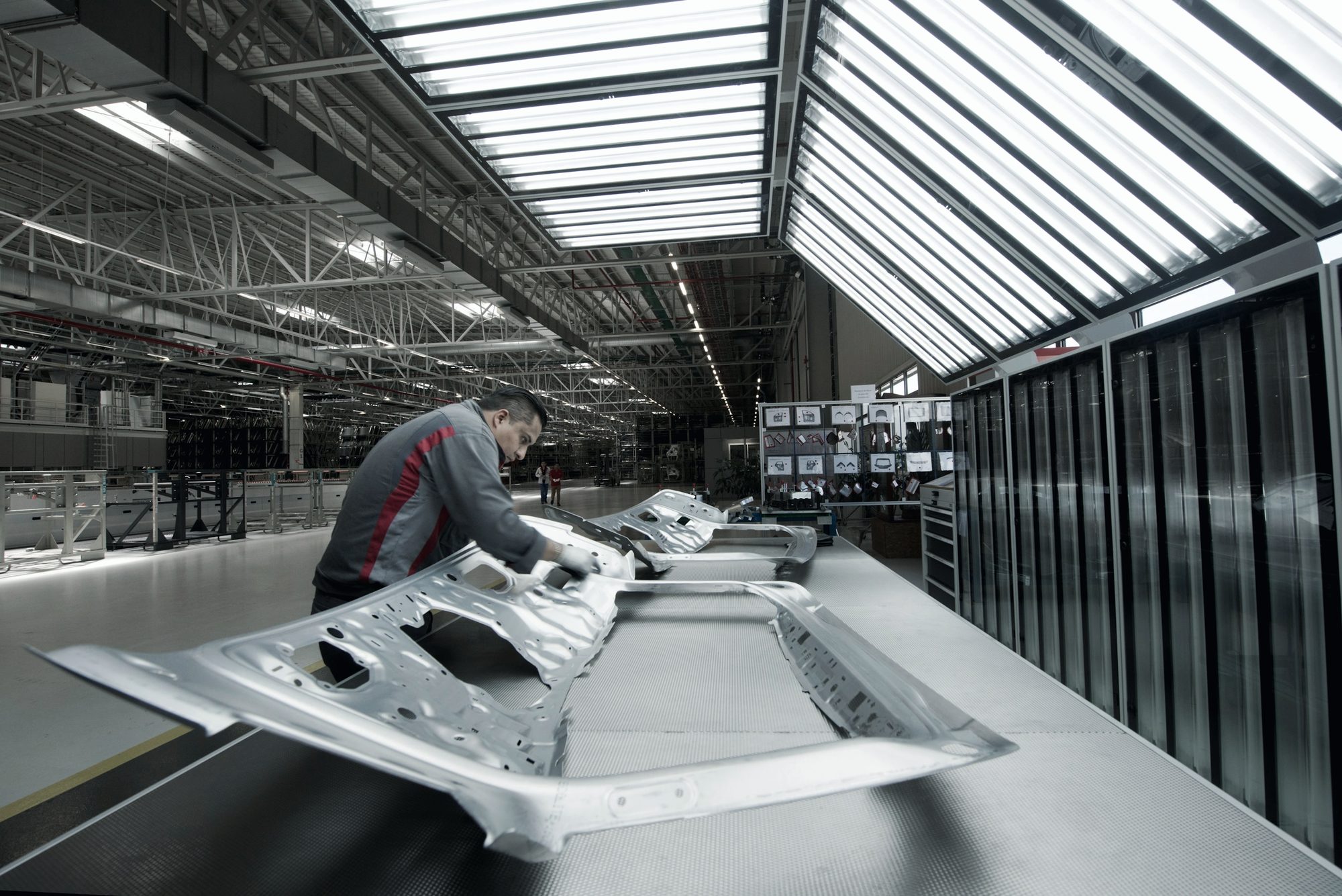 A technician inspecting vehicle body panels on a long, bright assembly hall floor