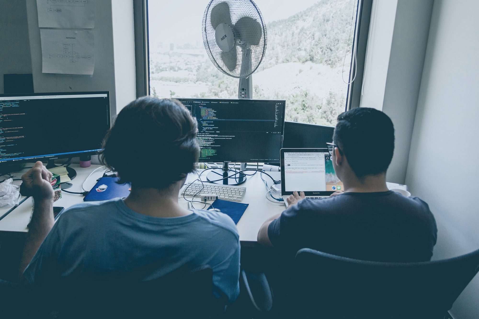 Two engineers working side by side at monitors full of code